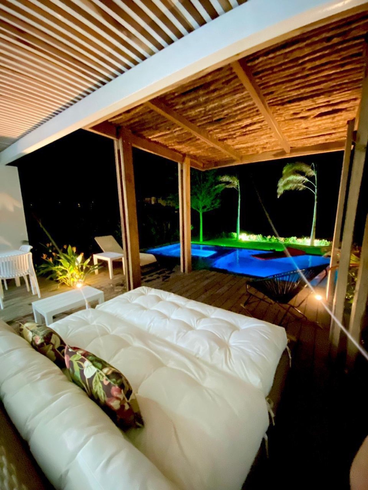 Terraza cubierta de noche, con daybed y piscina iluminada